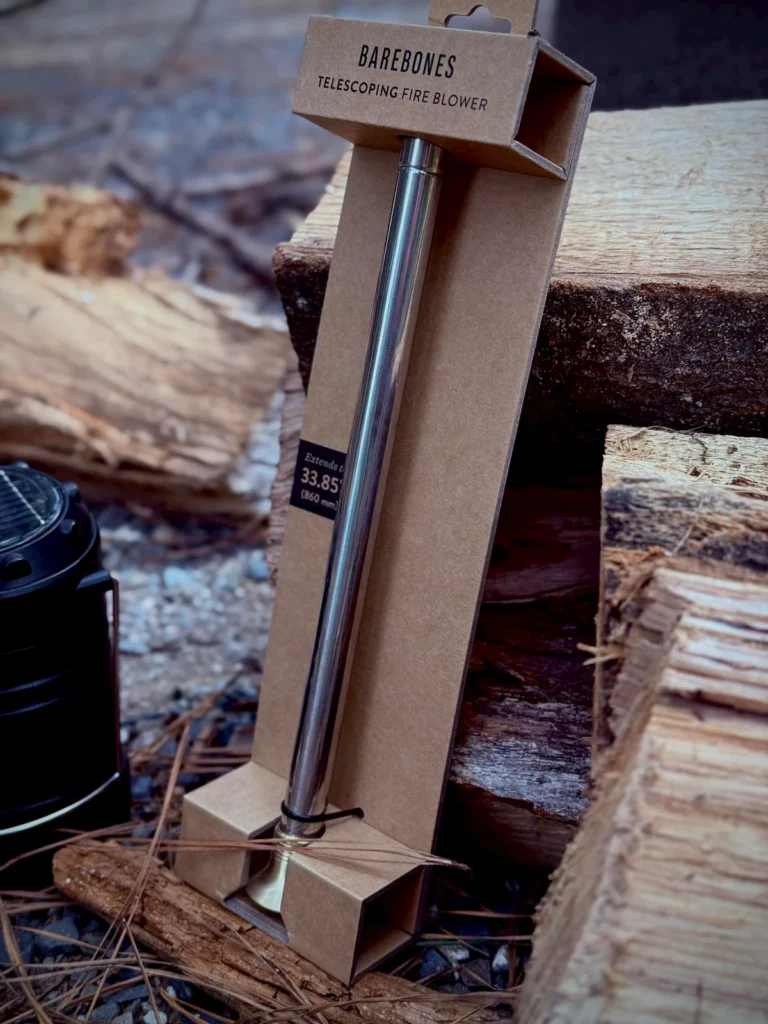 The Barebones Telescoping Fire Blower tool sitting on a stack of firewood