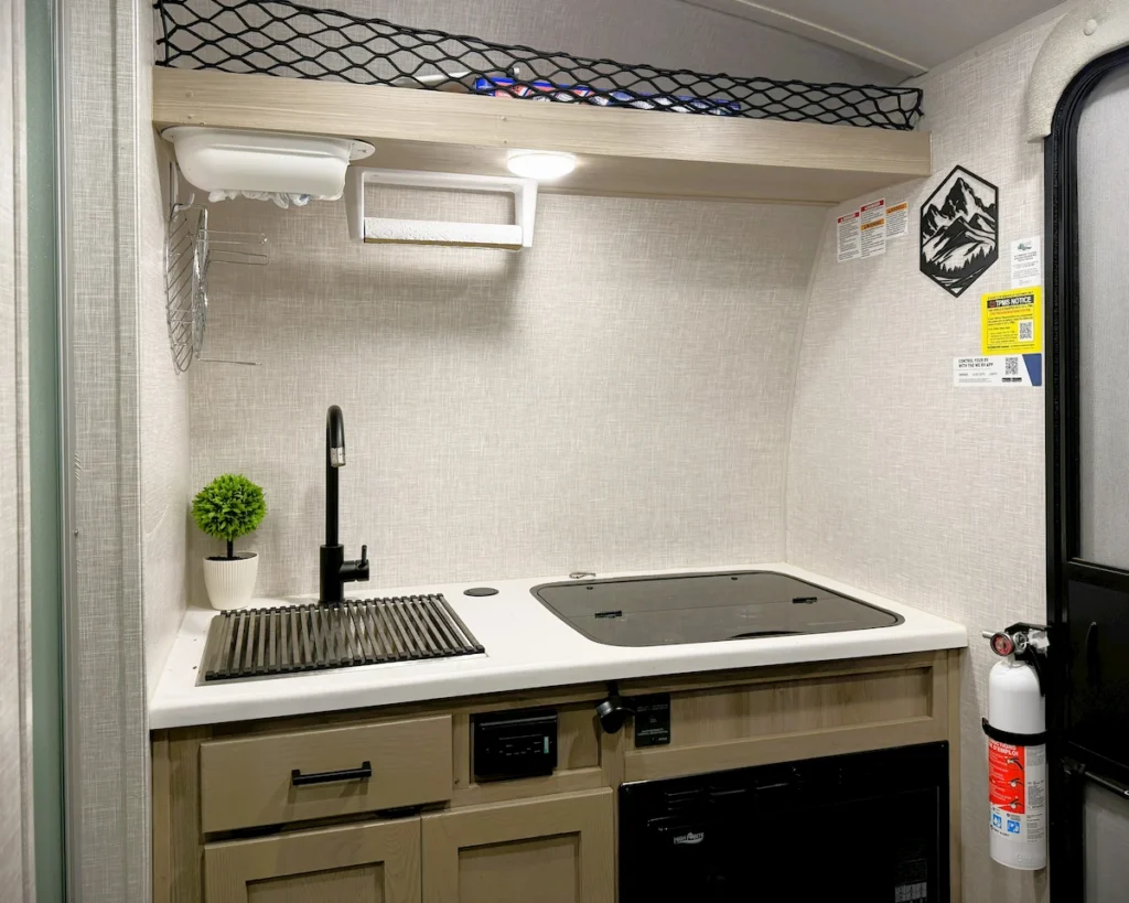 Interior view of the 2023 Flagstaff E-Pro 15TB kitchenette featuring the three-burner cooktop and microwave.