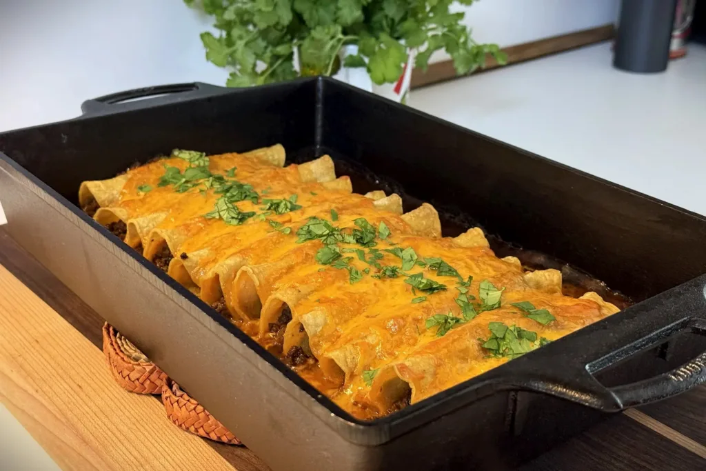 Cast Iron Enchiladas with melted cheddar cheese and fresh cilantro, baked to a crisp in a black Lodge 9x13 cast iron casserole dish.