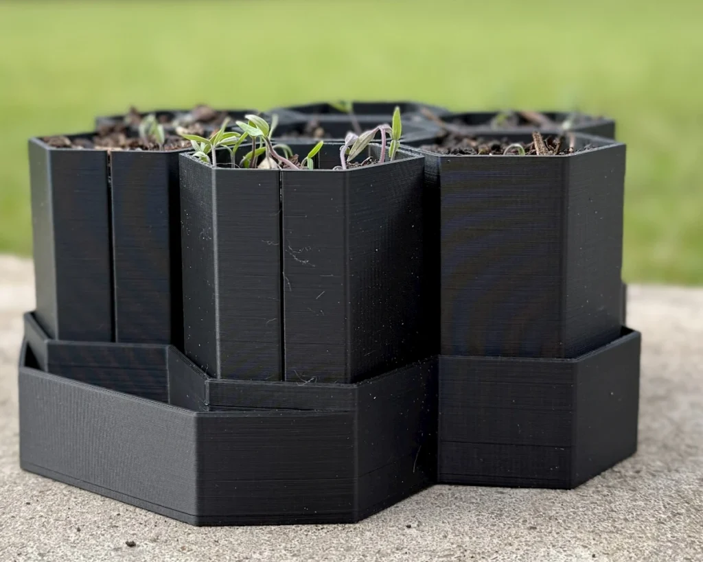 A close-up of custom 3D-printed snap-apart seed starter pods holding young plants for transplanting.