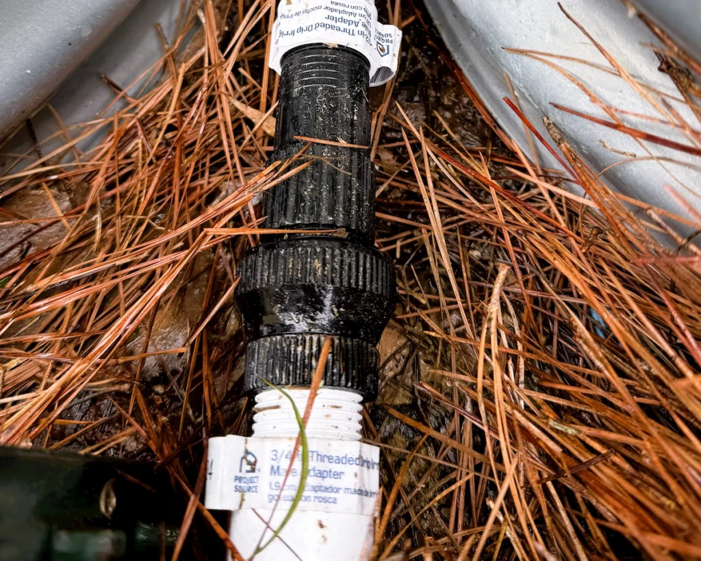 A drip irrigation backflow preventer and pressure regulator assembly attached to a PVC line for an automated irrigation system.