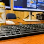 A close-up, angled shot of a computer keyboard with a computer monitor softly out of focus in the background, displaying a website page about the expn.pro Experian text scam.