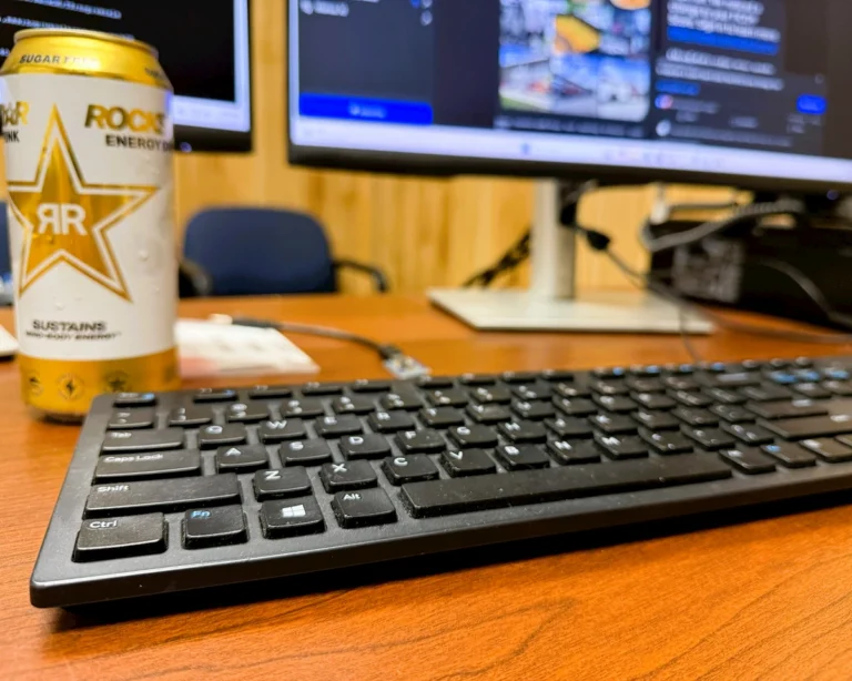 A close-up, angled shot of a computer keyboard with a computer monitor softly out of focus in the background, displaying a website page about the expn.pro Experian text scam.