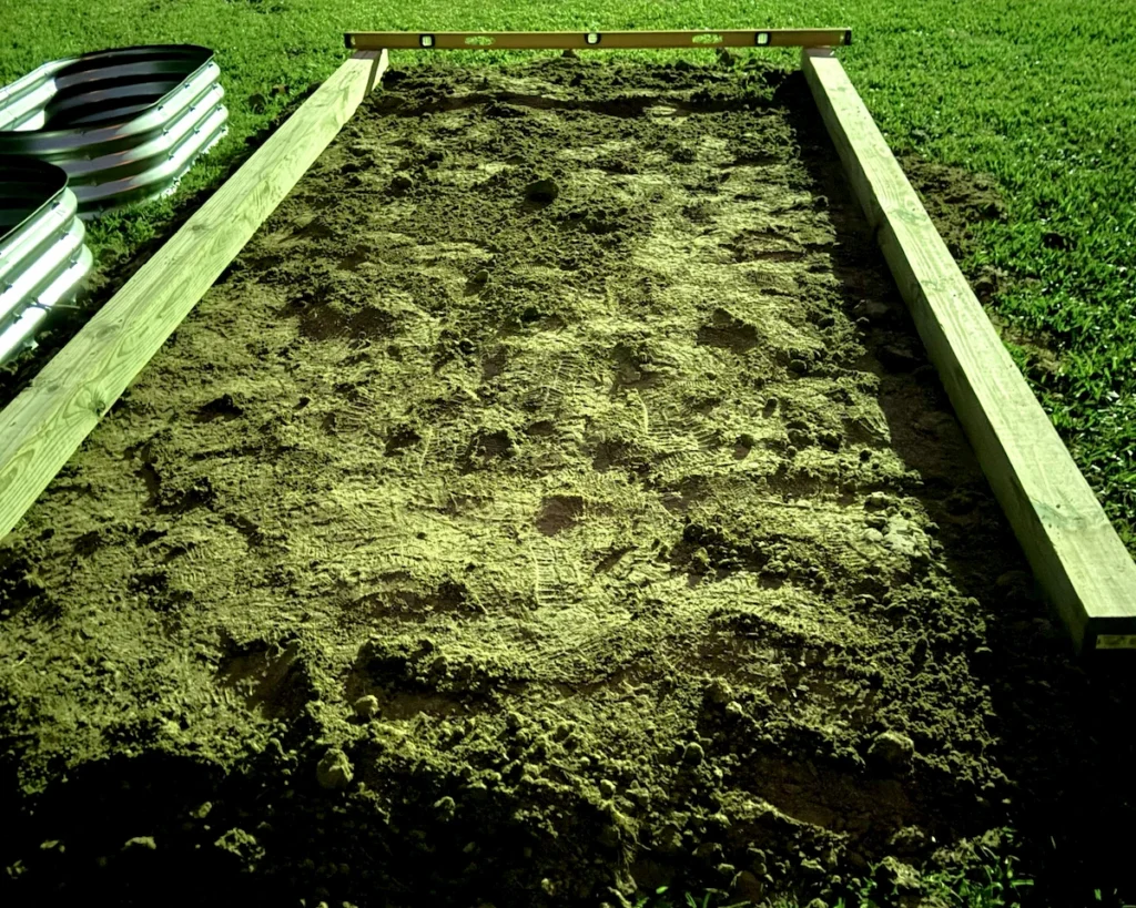 Two 4x4 timber posts laid across a leveled dirt pad at night with a carpenter level on top to check the grade.