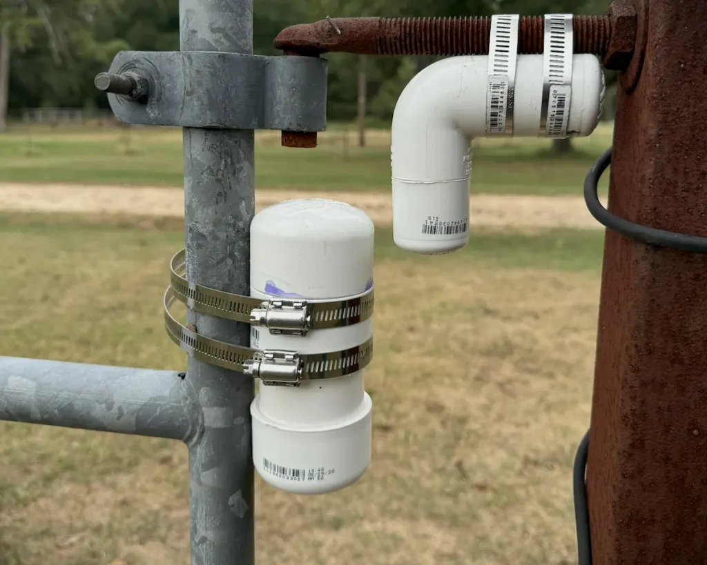 YoLink outdoor contact sensor housed inside a 2-inch PVC pipe mounted to a metal cattle gate frame with hose clamps.